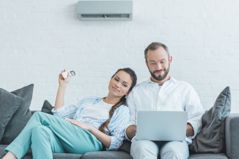 couple sitting on a couch turning on their ductless system with a remote.