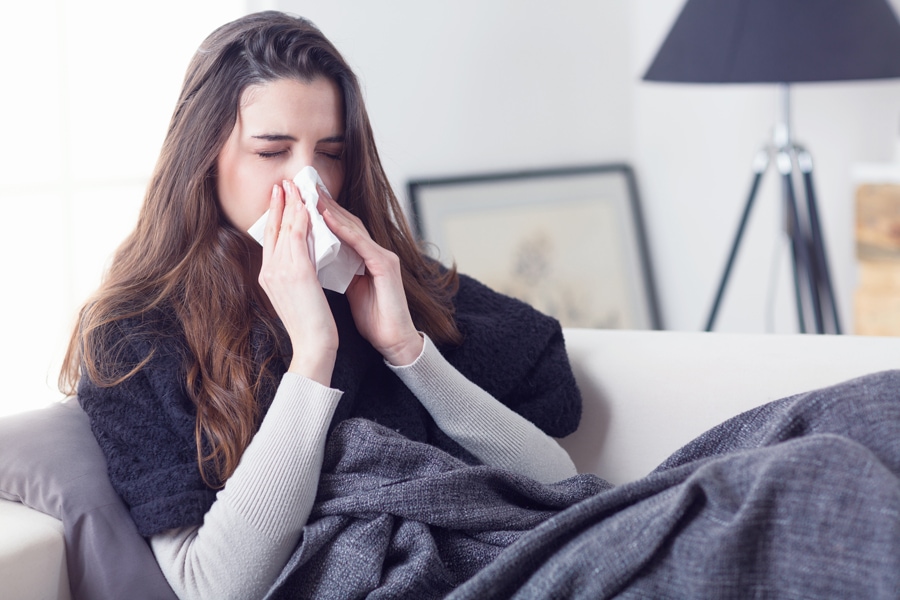 Young attractive woman lying sick at home couch in cold and flu sneezing nose with tissue covering with blanket