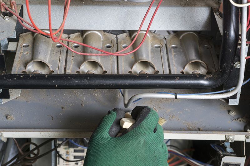 A person with a green glove examines a furnace. 5 Reasons to Schedule a Fall Furnace Clean and Check.